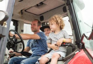 Un homme et deux enfants assis ensemble dans un tracteur à FarmCamps Op Flakkee, parc de vacances en Hollande-Méridionale, Pays-Bas.