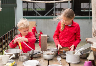 Deux enfants en rouge jouent dehors avec des casseroles chez FarmCamps Op Flakkee, Hollande méridionale.