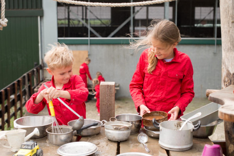 Dos niños vestidos de rojo juegan al aire libre con ollas y utensilios en FarmCamps Op Flakkee, Holanda del Sur.