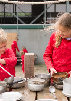 Dos niños vestidos de rojo juegan al aire libre con ollas y utensilios en FarmCamps Op Flakkee, Holanda del Sur.