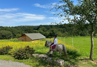 Barn rider på en plettet pony på en grøn mark ved FarmCamps Soodehof Eins, Hesse, Tyskland, om sommeren.