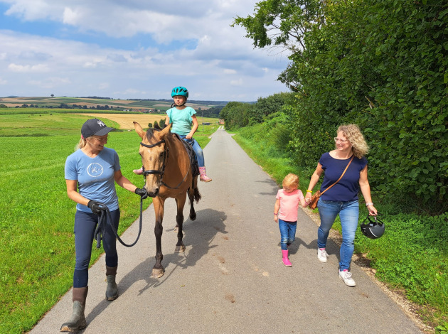 Twee vrouwen en twee kinderen, waarvan één op een paard, wandelen bij FarmCamps Soodehof Eins in Hesse.