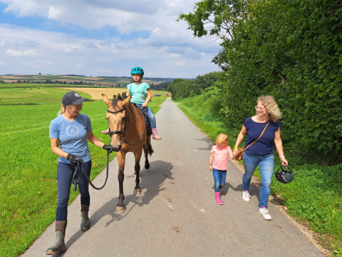 Dos mujeres y dos niños, uno montando a caballo, pasean juntos por un sendero rural en FarmCamps Soodehof Eins.