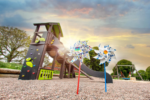 Bunte Spielplatz mit Rutsche, Schaukeln und Windrädern bei Sonnenuntergang im FarmCamps Soodehof Eins, Hessen.