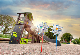 Bunte Spielplatz mit Rutsche, Schaukeln und Windrädern bei Sonnenuntergang im FarmCamps Soodehof Eins, Hessen.