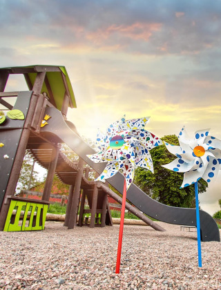 Bunte Spielplatz mit Rutsche, Schaukeln und Windrädern bei Sonnenuntergang im FarmCamps Soodehof Eins, Hessen.