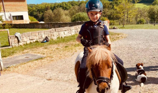 Ein Kind mit Helm reitet auf einem Pony bei FarmCamps Soodehof Eins in Hessen, Deutschland, an einem sonnigen Tag.