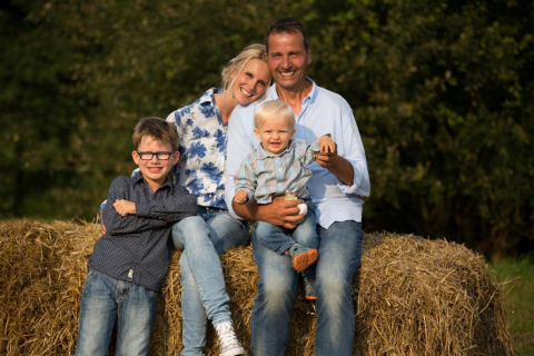 A happy family of four sits on hay bales outdoors at FarmCamps Soodehof Eins in Hesse, Germany.