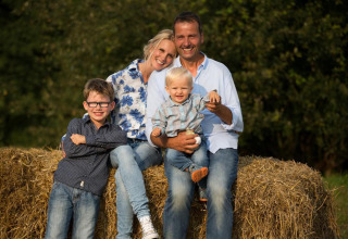 Une famille heureuse de quatre personnes assise sur des bottes de foin à FarmCamps Soodehof Eins, Hesse, Allemagne.
