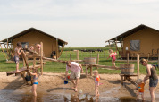 Børn og voksne leger ved vandlegeplads foran teltlodges på FarmCamps Stolkse Weide i Holland.