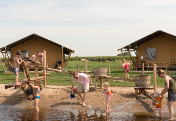 Børn og voksne leger ved vandlegeplads foran teltlodges på FarmCamps Stolkse Weide i Holland.