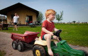 Et lille barn kører på en legetøjstraktor foran en hytte på FarmCamps Stolkse Weide i Sydholland.