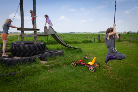 Kinder spielen auf einem Spielplatz mit Reifen, Rutsche und Schaukel im FarmCamps Stolkse Weide, Südholland.