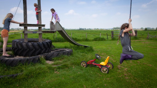 Kinderen spelen op een speelplaats met banden, glijbaan en schommel bij FarmCamps Stolkse Weide, Zuid-Holland.