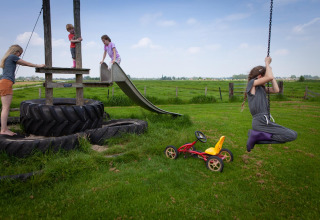 Kinderen spelen op een speelplaats met banden, glijbaan en schommel bij FarmCamps Stolkse Weide, Zuid-Holland.