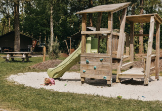 Bambino piccolo che gioca nella sabbia davanti allo scivolo del parco giochi a Camping het Horstmannsbos, Drenthe, Paesi Bassi.