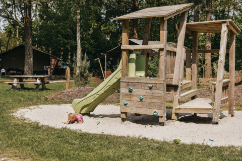 Niño pequeño jugando en la arena frente al tobogán del parque infantil en Camping het Horstmannsbos, Drenthe, Países Bajos.