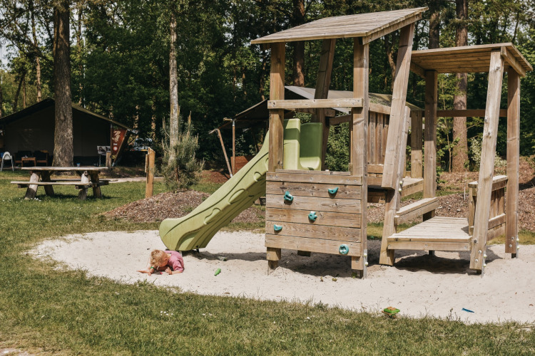 Kleines Kind spielt im Sand vor Spielplatz mit Rutsche auf Camping het Horstmannsbos in Drenthe, Niederlande.