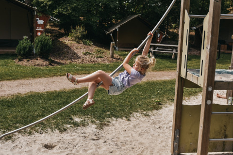 Ein Kind schwingt an einem Seil auf einem Spielplatz im Camping het Horstmannsbos, Drenthe, Niederlande.