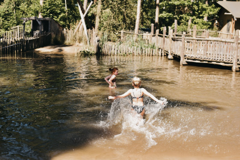 Zwei Kinder spielen im Wasser beim Camping het Horstmannsbos, umgeben von Bäumen und Holzzaun.