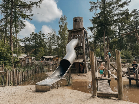 Kinder spielen auf einem Abenteuerspielplatz mit Rutsche und Hängebrücke in Camping het Horstmannsbos, Drenthe.