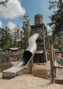Kinder spielen auf einem Abenteuerspielplatz mit Rutsche und Hängebrücke in Camping het Horstmannsbos, Drenthe.