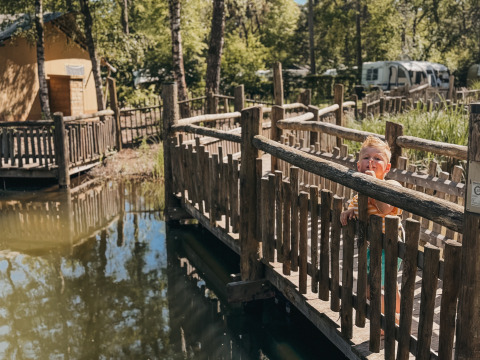 Kleines Kind auf einer Holzbrücke am Wasser im Camping het Horstmannsbos in Drenthe, Niederlande.