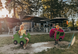 Two children play on playground rides near a café at Camping het Horstmannsbos, Drenthe, Netherlands.