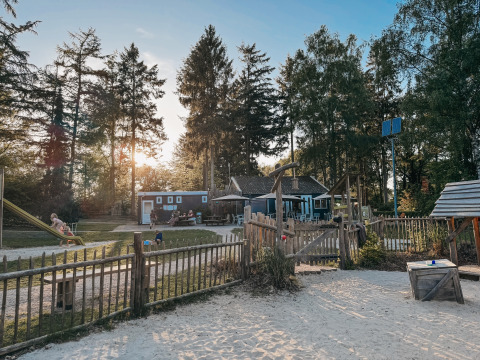 Playground and holiday park at Camping het Horstmannsbos in Drenthe, Netherlands, surrounded by trees at sunset.
