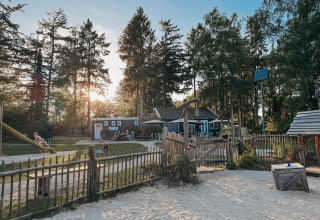 Parco giochi e area vacanze al Camping het Horstmannsbos a Drenthe, Paesi Bassi, circondati da alberi al tramonto.