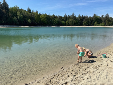 Children playing on the sandy shore of a lake at Camping het Horstmannsbos, Drenthe, Netherlands, with trees.