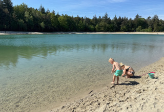 Kinderen spelen aan de zandige oever van het meer bij Camping het Horstmannsbos in Drenthe, omringd door bos.