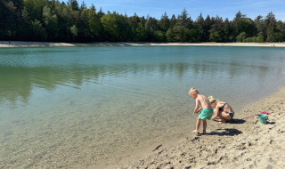 Niños juegan en la orilla arenosa de un lago en Camping het Horstmannsbos, Drenthe, Países Bajos, rodeados de árboles.