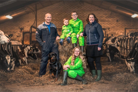 Familie mit Hund auf Heuballen inmitten von Kühen in einem Stall bei FarmCamps Stolkse Weide, Südholland.