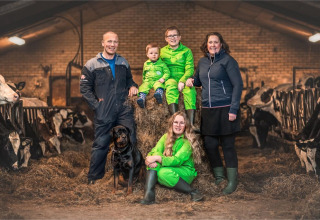 Familie mit Hund auf Heuballen inmitten von Kühen in einem Stall bei FarmCamps Stolkse Weide, Südholland.