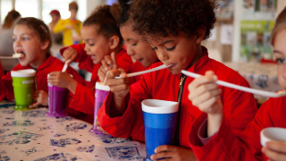 Kinderen in rode outfits drinken plezierig met lange rietjes op FarmCamps Stolkse Weide, Zuid-Holland.