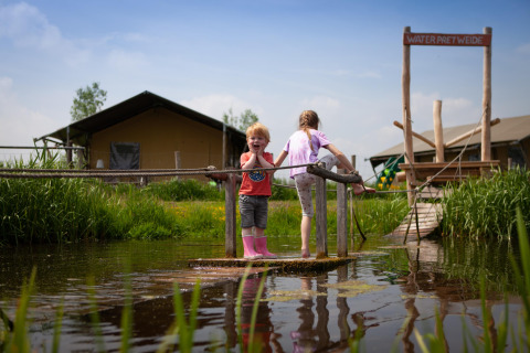 Zwei Kinder spielen auf einem Floß auf dem Wasser bei FarmCamps Stolkse Weide in Südholland, Niederlande.