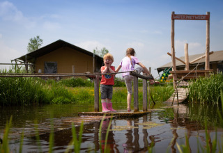 Twee kinderen spelen op een vlot op het water bij FarmCamps Stolkse Weide, een vakantiepark in Zuid-Holland.