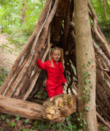 Niña con mono rojo explora un refugio hecho de ramas en el bosque de FarmCamps De Verloren Kost, Limburg.