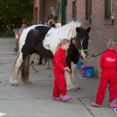 Dos niños con monos rojos junto a un caballo blanco y negro en FarmCamps De Verloren Kost en Limburgo.