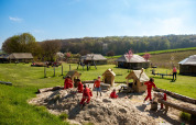 Kinder spielen in einem Sandkasten auf FarmCamps De Verloren Kost mit Wiesen und Zelten im Hintergrund.