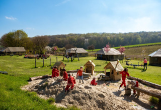 Children playing in a large sandbox at FarmCamps De Verloren Kost with grassy fields and tents behind them.