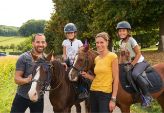 En glad familie med to børn og voksne nyder ridning på heste ved FarmCamps De Verloren Kost i Limburg.