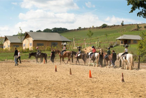 Des enfants en cours d'équitation à FarmCamps De Verloren Kost, Limbourg, Pays-Bas, avec tentes au fond.