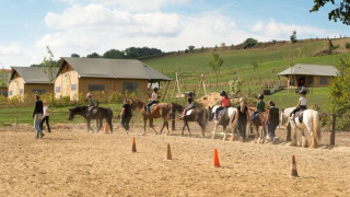 Niños tomando clases de equitación en FarmCamps De Verloren Kost en Limburgo, Países Bajos, con tiendas.