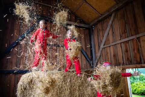 Niños juegan felices en la paja con trajes rojos dentro de un granero en FarmCamps Fleur Stables, Países Bajos.
