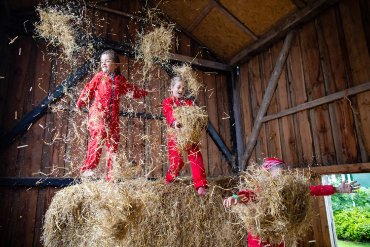 Children playing joyfully in hay wearing red jumpsuits inside a barn at FarmCamps Fleur Stables, Netherlands.