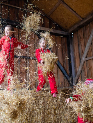 Niños juegan felices en la paja con trajes rojos dentro de un granero en FarmCamps Fleur Stables, Países Bajos.
