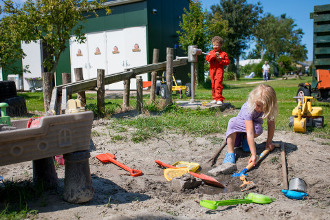 Bambini giocano con giocattoli nella sabbia a FarmCamps Fleur Stables, parco vacanze in Olanda Settentrionale.