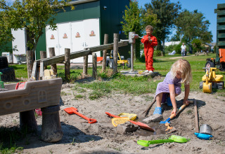 Børn leger i en sandkasse med legetøj på FarmCamps Fleur Stables feriested i Nordholland, Holland.